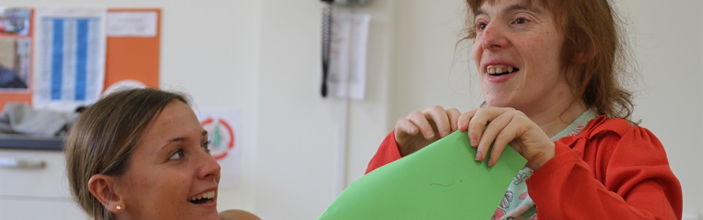 Smiling care worker and woman with learning disabilities doing arts and crafts